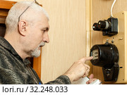 The man takes the readings of the apartment electric meter and writes it in the notebook. Стоковое фото, фотограф Акиньшин Владимир / Фотобанк Лори