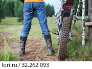 Male rider well shod in protective boots standing near off-road motorcycle on dirt road, rear view. Стоковое фото, фотограф Кекяляйнен Андрей / Фотобанк Лори