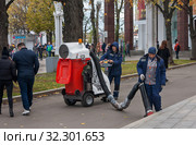 Двое рабочих в синей спецодежде убирают тротуар на ВДНХ в Москве с помощью уличного пылесоса (2019 год). Редакционное фото, фотограф Наталья Николаева / Фотобанк Лори