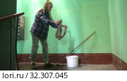 A young woman in blue jeans and a cage shirt swings and washes the floor on a staircase next to an elevator in a Stalinist-built apartment building, Cleaning public spaces by a labor immigrant cleane. Стоковое видео, видеограф Куликов Константин / Фотобанк Лори