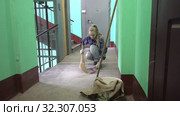 A young woman in blue jeans and a cage shirt swings and washes the floor on a staircase next to an elevator in a Stalinist-built apartment building, Cleaning public spaces by a labor immigrant cleane. Стоковое видео, видеограф Куликов Константин / Фотобанк Лори