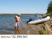 Только что пойманного сазана мужчина держит на кукане в воде на фоне реки ясным днём (2019 год). Редакционное фото, фотограф Игорь Низов / Фотобанк Лори