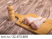 Raw chicken legs on a cutting board and peppercorns with pepper mill. On wooden table. Стоковое фото, фотограф Юлия Бабкина / Фотобанк Лори