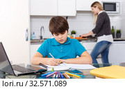 Boy doing homework, mother cooking. Стоковое фото, фотограф Яков Филимонов / Фотобанк Лори