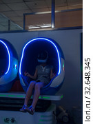 China, Heihe, July 2019: a Girl plays virtual reality in a futuristic cockpit (capsule) in the Huafu shopping center. Редакционное фото, фотограф Катерина Белякина / Фотобанк Лори