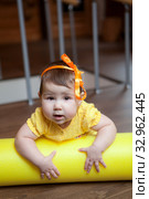 Baby girl lying on yellow foam roller in domestic gym, looking at camera. Стоковое фото, фотограф Кекяляйнен Андрей / Фотобанк Лори