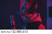 A man in headphones rapping through the pop-filter in the microphone - sound recording studio in neon lighting. Стоковое видео, видеограф Константин Шишкин / Фотобанк Лори