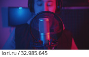 A man in hoodie rapping through the pop-filter in the microphone - recording his track in the studio. Стоковое видео, видеограф Константин Шишкин / Фотобанк Лори
