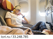 Tired blonde casual caucasian lady napping on uncomfortable seat while traveling by airplane. Стоковое фото, фотограф Matej Kastelic / Фотобанк Лори