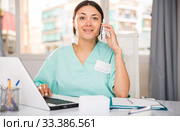 Practicioner woman in medical uniform talking by phone at laptop. Стоковое фото, фотограф Яков Филимонов / Фотобанк Лори