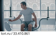 Modern gym - young guy sitting down on the training apparatus and waiting for when it will be possible to start. Стоковое видео, видеограф Константин Шишкин / Фотобанк Лори
