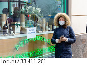 Девушка в медицинской маске около витрины аптеки с объявлением "Маски в наличии" (2020 год). Редакционное фото, фотограф Светлана Голинкевич / Фотобанк Лори