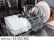 Large and small white plates, steel forks, spoons in open dishwasher. Стоковое фото, фотограф Кекяляйнен Андрей / Фотобанк Лори