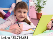 Счастливая школьница дистанционно учится дома, лежит в кровати и радостно посмотрела в кадр. Стоковое фото, фотограф Иванов Алексей / Фотобанк Лори