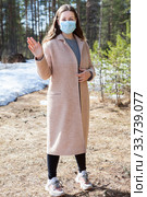 Caucasian woman waving with the hand, standing in the spring forest wearing medical mask, full length portrait. Стоковое фото, фотограф Кекяляйнен Андрей / Фотобанк Лори
