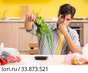Young man calculating expences for vegetables in kitchen. Стоковое фото, фотограф Elnur / Фотобанк Лори