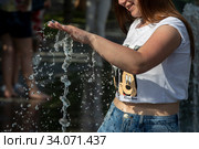 Молодая девушка трогает струю фонтана в парке Музеон на Крымской набережной во время изнуряющей жары в городе Москве, Россия (2020 год). Редакционное фото, фотограф Николай Винокуров / Фотобанк Лори