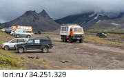Lots of SUVs and passenger trucks driving and parked along mountain road at foot of volcano in dramatic cloudy weather, volcanic landscape (2019 год). Редакционное фото, фотограф А. А. Пирагис / Фотобанк Лори