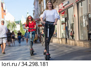 Trendy fashinable teenager girls riding public rental electric scooters in urban city environment. New eco-friendly modern public city transport in Ljubljana, Slovenia. Стоковое фото, фотограф Matej Kastelic / Фотобанк Лори