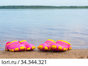 Детские розовые сабо стоят на песчаном пляже около воды. Стоковое фото, фотограф Мария / Фотобанк Лори