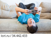 Portrait of Caucasian teenager with large smartphone or game console in hands, playing or engaging over social media while lying his back on sofa. Стоковое фото, фотограф Кекяляйнен Андрей / Фотобанк Лори