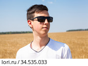 Teenage Caucasian boy portrait wearing black sunglasses, man standing on a wheat field at sunny day, white t-shirt. Стоковое фото, фотограф Кекяляйнен Андрей / Фотобанк Лори