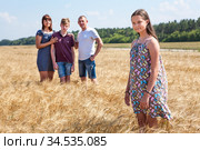 Concept of adopted child, young girl standing on foreground with adoptive family on background, stepdaughter with father, mother and brother. Стоковое фото, фотограф Кекяляйнен Андрей / Фотобанк Лори