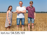 Pre-teen son and daughter with their single father, kids lay hands on his shoulders, looking at camera, full length portrait at wheat field. Стоковое фото, фотограф Кекяляйнен Андрей / Фотобанк Лори