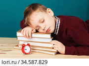 tired school boy asleep on books. little student sleeping on textbooks. Child in school uniform lies on the table with big pile of books against blue wall. Eyes closed. Back to school. Стоковое фото, фотограф Nataliia Zhekova / Фотобанк Лори