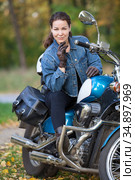 Curly woman sitting on her chopper motorbike on urban park, female wearing jeans jacket and leather gloves. Стоковое фото, фотограф Кекяляйнен Андрей / Фотобанк Лори
