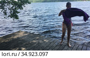 Caucasian teenage girl gets out from the water on wooden pier and wipes with towel, forest lake at summer season. Стоковое видео, видеограф Кекяляйнен Андрей / Фотобанк Лори