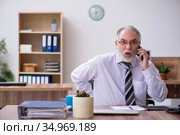 Old male employee suffering from radiculitis at workplace. Стоковое фото, фотограф Elnur / Фотобанк Лори