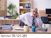 Old male employee suffering from radiculitis at workplace. Стоковое фото, фотограф Elnur / Фотобанк Лори