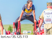 Russia, Samara, June 2019: a young beautiful athlete moves through red pipes overcoming the distance of the heroes race on a summer sunny day. Text in Russian: race of heroes, platoon, judge. Редакционное фото, фотограф Акиньшин Владимир / Фотобанк Лори