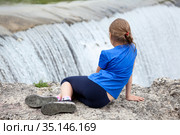 Rear view at preteen age girl sitting on edge of waterfall of the Cijevna river. It is called Montenegrin Niagara Falls. Surroundings of Podgorica city. Montenegro, Europe. Стоковое фото, фотограф Кекяляйнен Андрей / Фотобанк Лори