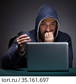 Young man wearing a hoodie sitting in front of a laptop computer. Стоковое фото, фотограф Elnur / Фотобанк Лори