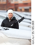 Caucasian woman looking from the snowy car hood, female driver holding snow brush in hand. Стоковое фото, фотограф Кекяляйнен Андрей / Фотобанк Лори