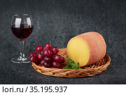 Delicious tete de moine cheese in a flat basket with grapevine next to a glass of wine. Traditional Swiss cheese. Стоковое фото, фотограф Алексей Голованов / Фотобанк Лори