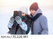 Two happy women friends sharing a smart phone after photo self shooting in cold winter lake shore. Стоковое фото, фотограф Кекяляйнен Андрей / Фотобанк Лори