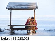 Two frozen women wrapping with red scarf sitting on wooden bench, talking and drinking hot beverages in thermo cups for warm up, winter seacoast. Стоковое фото, фотограф Кекяляйнен Андрей / Фотобанк Лори