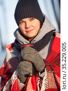 Attractive young Caucasian woman dressing woollen hat and mittens, wrapping in scarf holding thermo cup in hands, close up portrait. Стоковое фото, фотограф Кекяляйнен Андрей / Фотобанк Лори