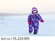Toddler girl dressing windproof snowsuit with hood running on snow field at winter season. Стоковое фото, фотограф Кекяляйнен Андрей / Фотобанк Лори