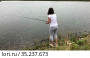 Attractive woman standing on lake shore with rod in hands, female fisher is on recreational fishing. Стоковое видео, видеограф Кекяляйнен Андрей / Фотобанк Лори