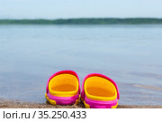 Детские розовые сабо стоят на песчаном пляже около воды. Children's pink clogs stand on a sandy beach near the water. Стоковое фото, фотограф Мария / Фотобанк Лори