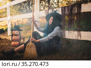 Ведьма сидит у забора на ферме и метлой раздувает дым. Стоковое фото, фотограф Иванов Алексей / Фотобанк Лори