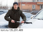Adult man a driver sweeps snow from hood of car with brush, portrait at winter time. Стоковое фото, фотограф Кекяляйнен Андрей / Фотобанк Лори