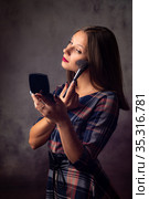 Девушка пудрит кистью лицо смотрясь в зеркальце, студийная фотография на сером фоне. Стоковое фото, фотограф Иванов Алексей / Фотобанк Лори