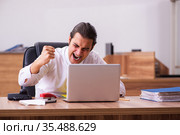 Young male employee stapling paper in the office. Стоковое фото, фотограф Elnur / Фотобанк Лори
