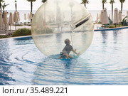 Little boy have fun inside big plastic balloon on the water of swimming pool on the summer resort. Kid inside big inflatable transparent ball running and having fun. Стоковое фото, фотограф Nataliia Zhekova / Фотобанк Лори
