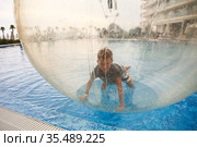 Little boy have fun inside big plastic balloon on the water of swimming pool on the summer resort. Kid inside big inflatable transparent ball running and having fun. Стоковое фото, фотограф Nataliia Zhekova / Фотобанк Лори